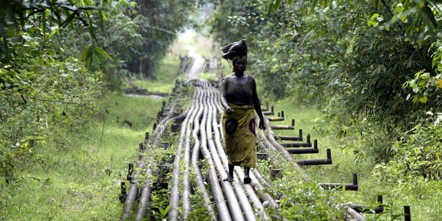 FILE- A woman walks along an oil pipeline in Warri, Nigeria, on Jan. 15, 2006. Nigerian state gas company has declared a force majeure after floods hindered gas operations, raising concerns among analysts about the West African nation's capacity to meet local and international demands. (AP Photo/George Osodi, File)