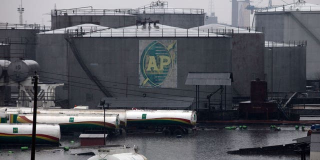 FILE- A tank farm and oil trucks are half submerged after a downpour at an oil terminal in Lagos Nigeria, on July. 11, 2011. Nigerian state gas company has declared a force majeure after floods hindered gas operations, raising concerns among analysts about the West African nation's capacity to meet local and international demands. (AP Photo/Sunday Alamba, File)