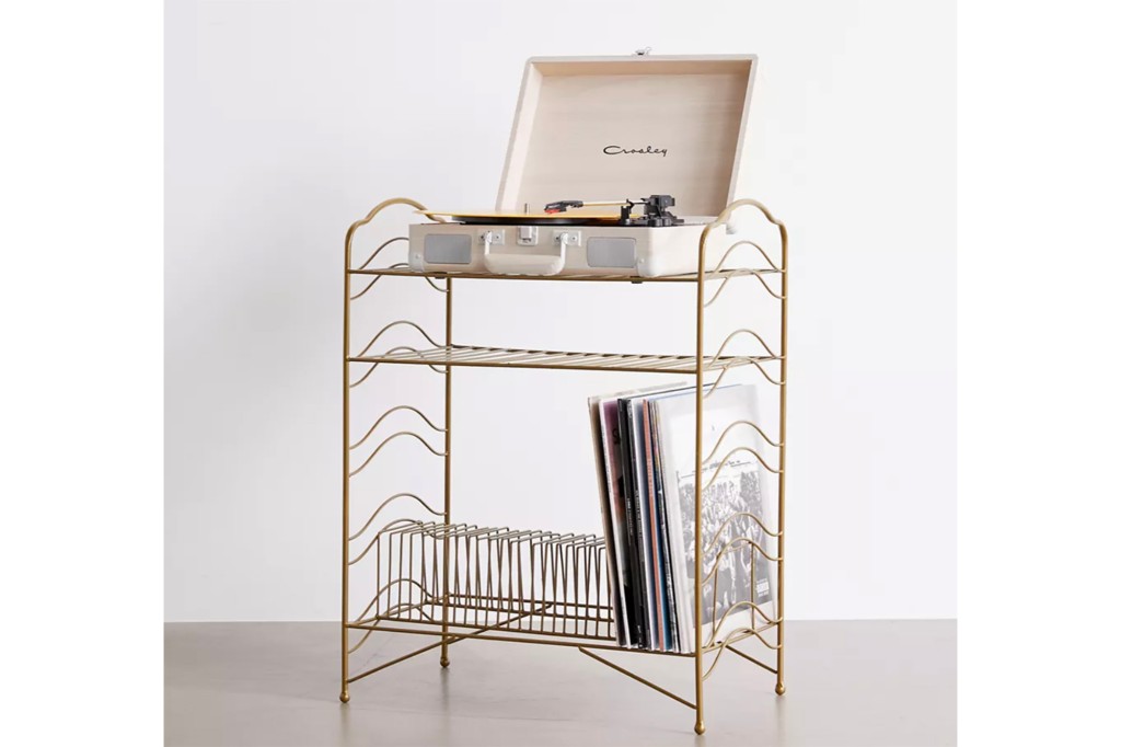 A gold shelf with a record player on top and records at the bottom 
