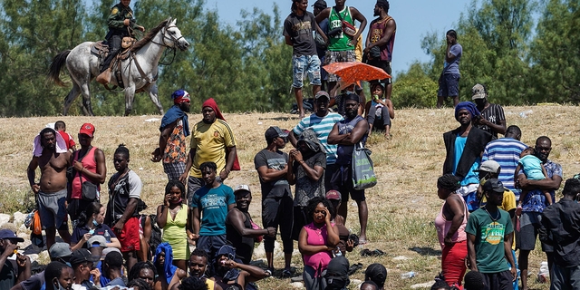 U.S. Border Patrol agents on horseback look on as Haitian migrants sit on the banks of the Rio Grande near the Acuna Del Rio International Bridge in Del Rio, Texas, on Sept. 19, 2021.