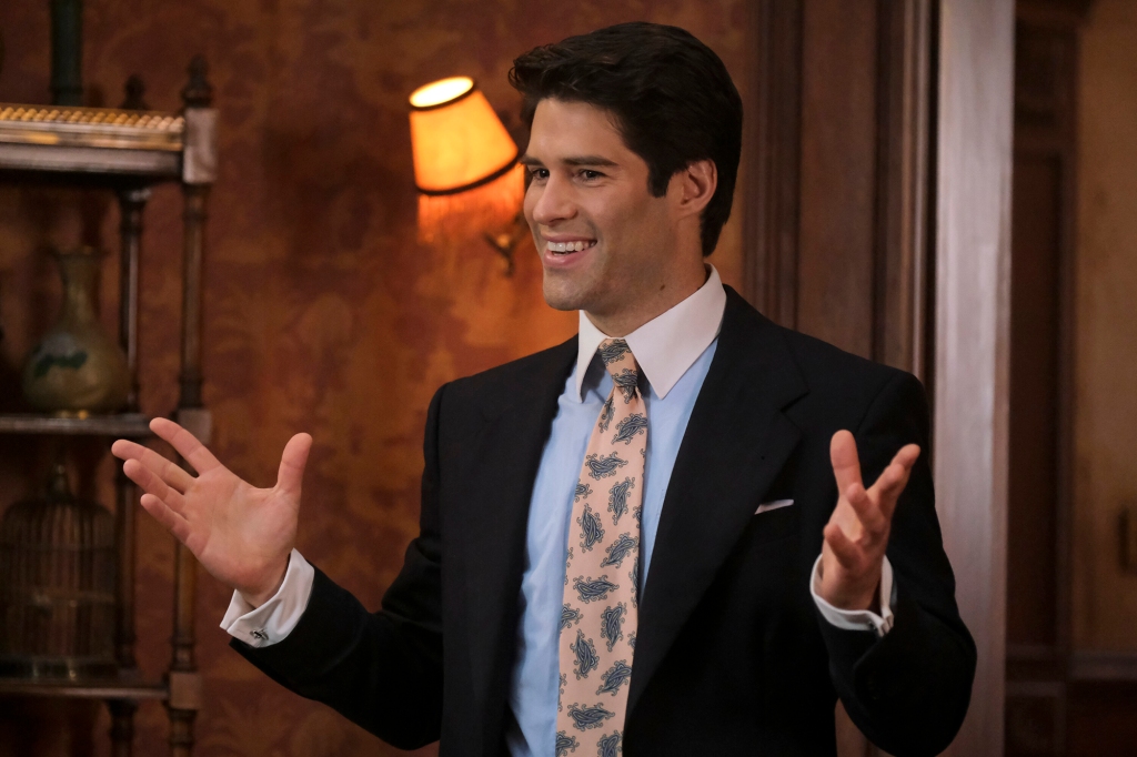 Asher Grodman as Trevor. He's wearing an '80s-era business suit with a pink power tie and is gesturing with his hands and has a big smile on his face.