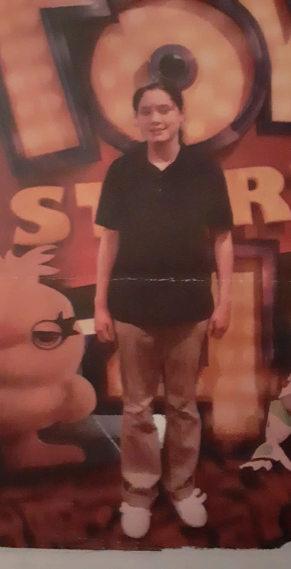 Cora Sepulvado in front of a Toy Story sign, looking at the camera and wearing a black polo shirt and khaki pants.