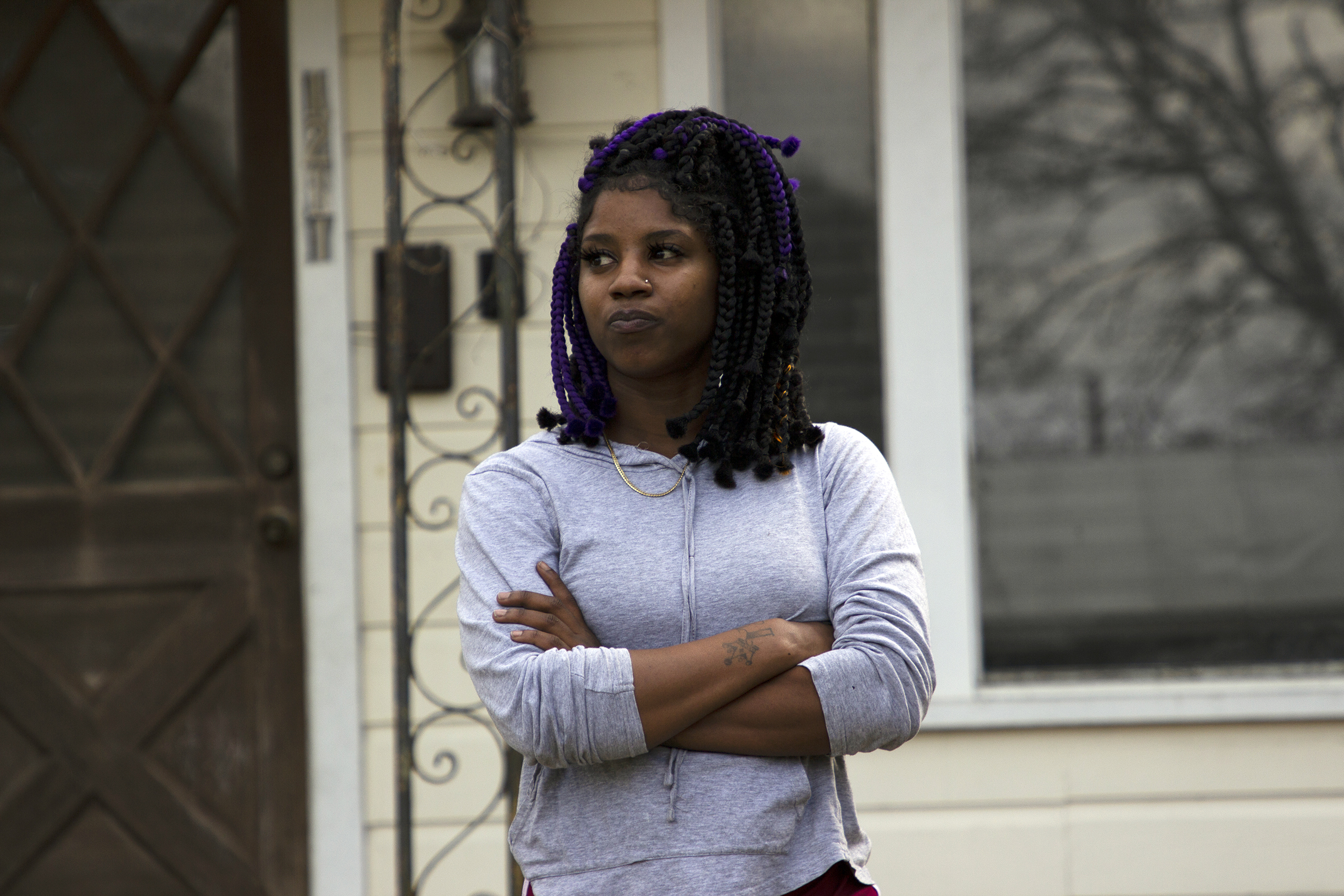 Gabryell Hardy standing in front of an off-white house. She wears a gray top and is crossing her arms and looking to the left.