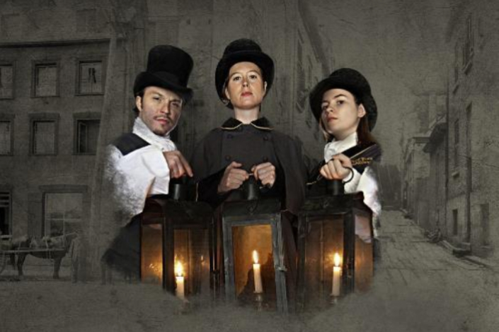 A trio of people in Victorian costumes and top hats holding lanterns