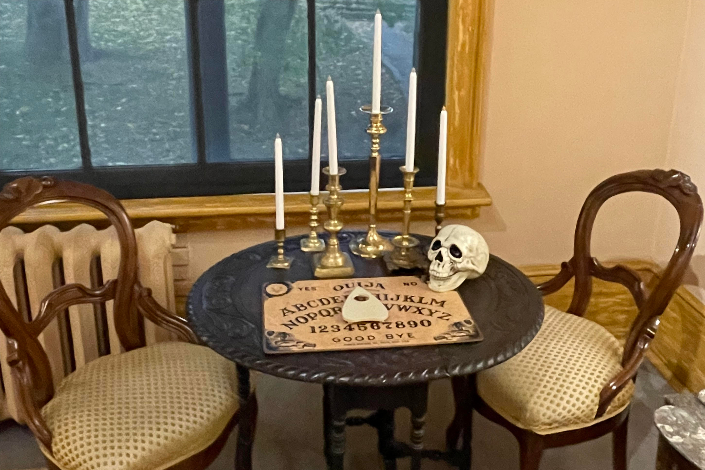 A table with Ouija board, candelabra, skull and two chairs