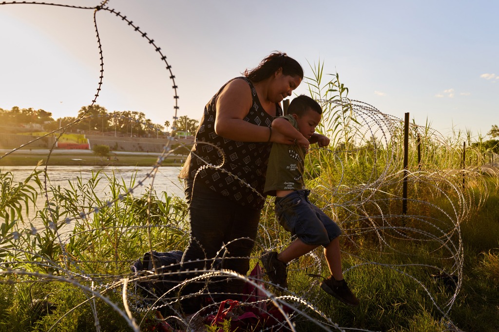 Analy Portillo Alarcon, of Managua, Nicaragua, lifts her son,  Luiz, 5, over razor wire after crossing the United States-Mexico border at the Rio Grande river on Saturday, July 23, 2022 in Eagle Pass, Texas. 