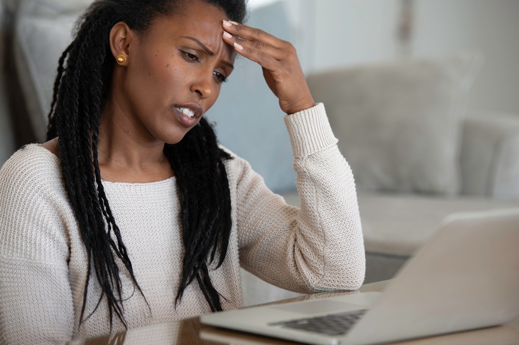 A woman touching a forehead while working on her laptop.