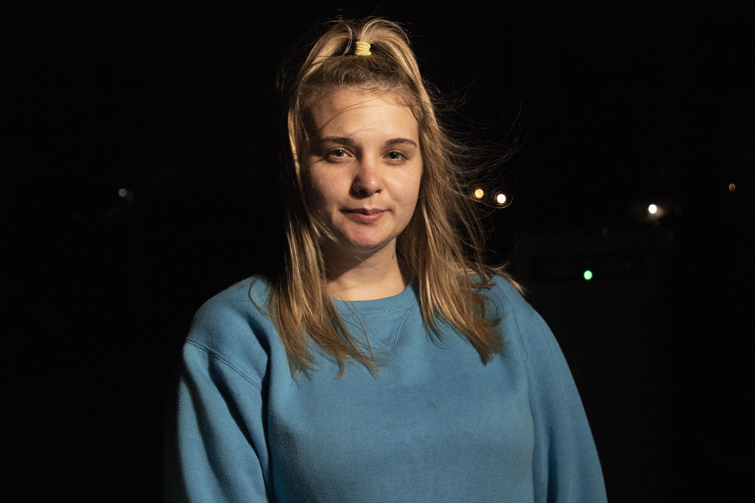 Kaley Breaux against a mostly dark background, with dots of light behind her. She is wearing a teal sweatshirt and looking into the camera.