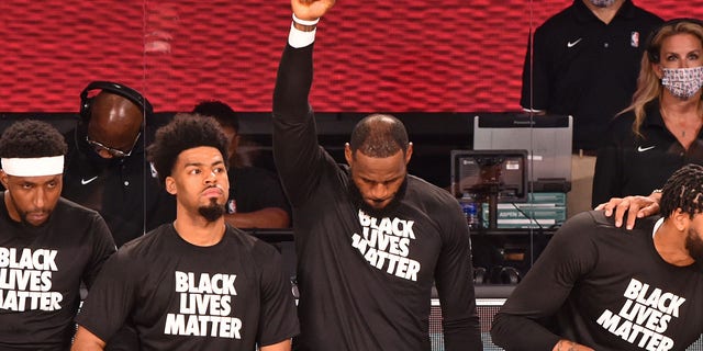 LeBron James of the Los Angeles Lakers raises his fist while kneeling for the national anthem before a game against the LA Clippers July 30, 2020, in Orlando, Fla.