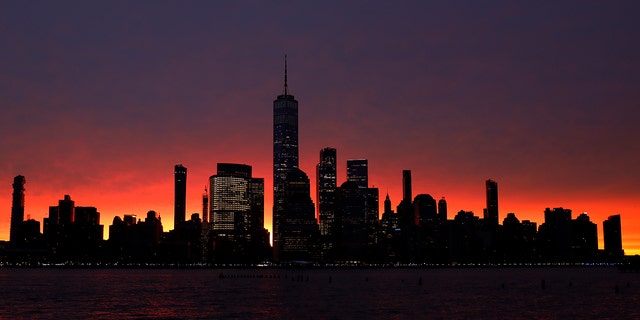 The sun rises behind the skyline of lower Manhattan and One World Trade Center in New York City.