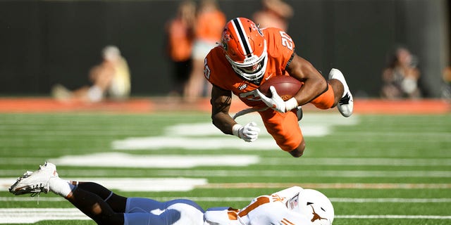 Oklahoma State running back Dominic Richardson (20) launches himself over Texas defensive back Anthony Cook, bottom, during the first half of an NCAA college football game Saturday, Oct. 22, 2022, in Stillwater, Okla.