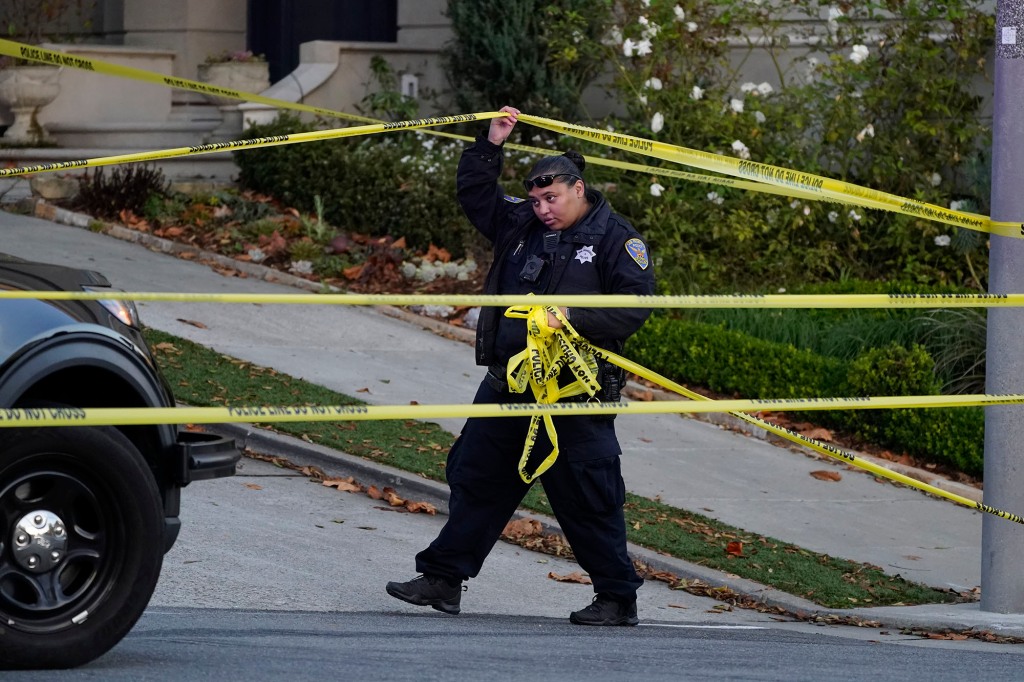 A police officer rolls out more yellow tape on the closed street below the home of Paul Pelosi.