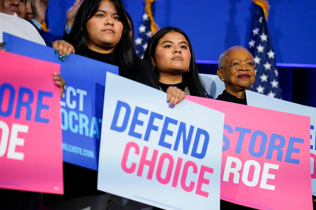 People hold signs on stage as President Joe Biden speaks about abortion