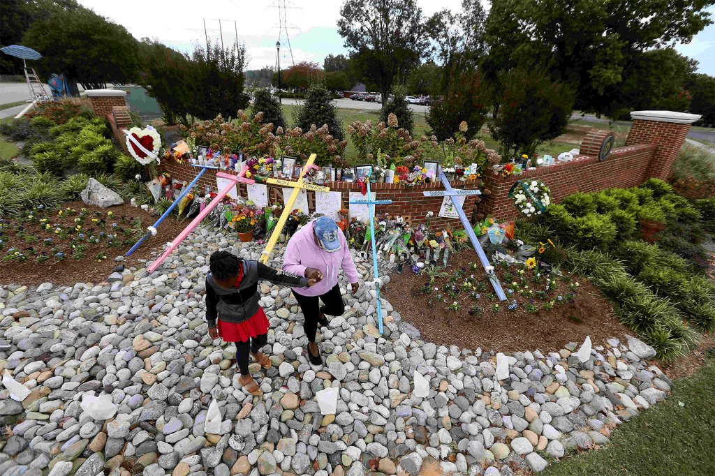 A woman holds hands with a little girl in front of a memorial site for the victims killed in the Hedingham neighborhood on Oct. 17, 2022.