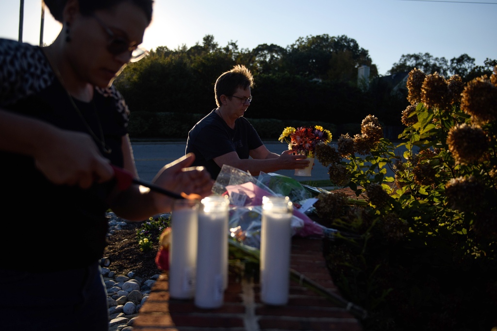 A woman lays flowers while another lights candles at the entrance of Hedingham neighborhood.