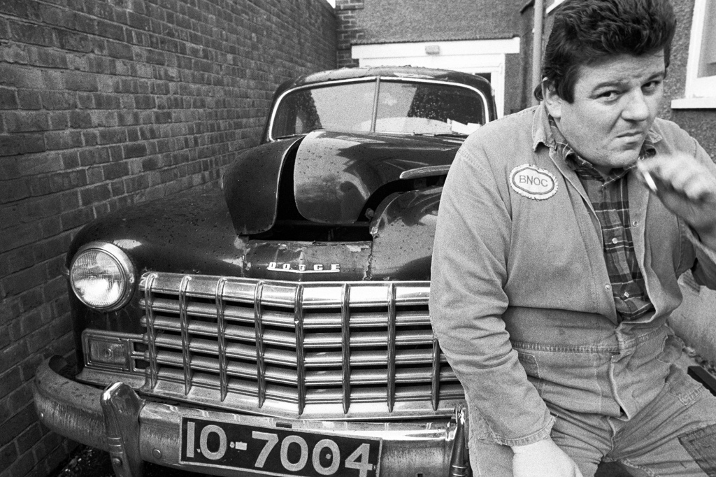 Robbie Coltrane at his home in Kilburn with his Dodge car, London, 1980.