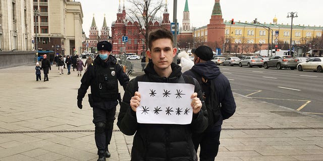 Police officers prepare to detain Dmitry Reznikov, who is holding a blank piece of paper with eight asterisks that could have been interpreted as standing for "No to war" in Moscow, Russia, on March 13, 2022.