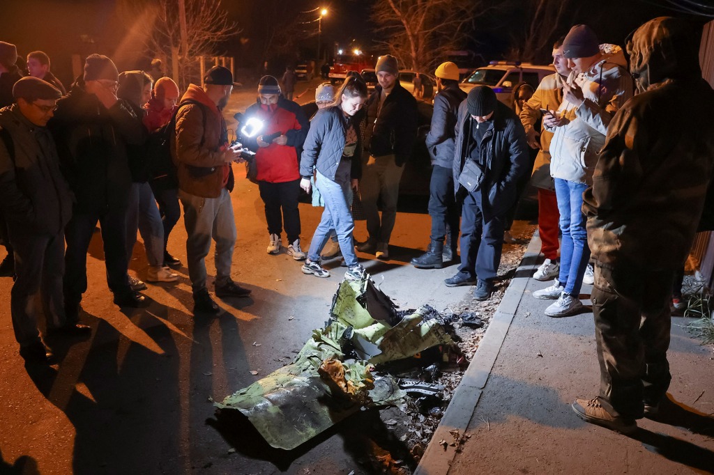 People gather around remains of a military plane at the site where it crashed into a residential building.