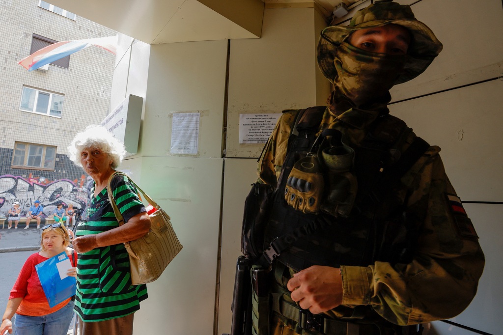 A soldier stands next to two civilians