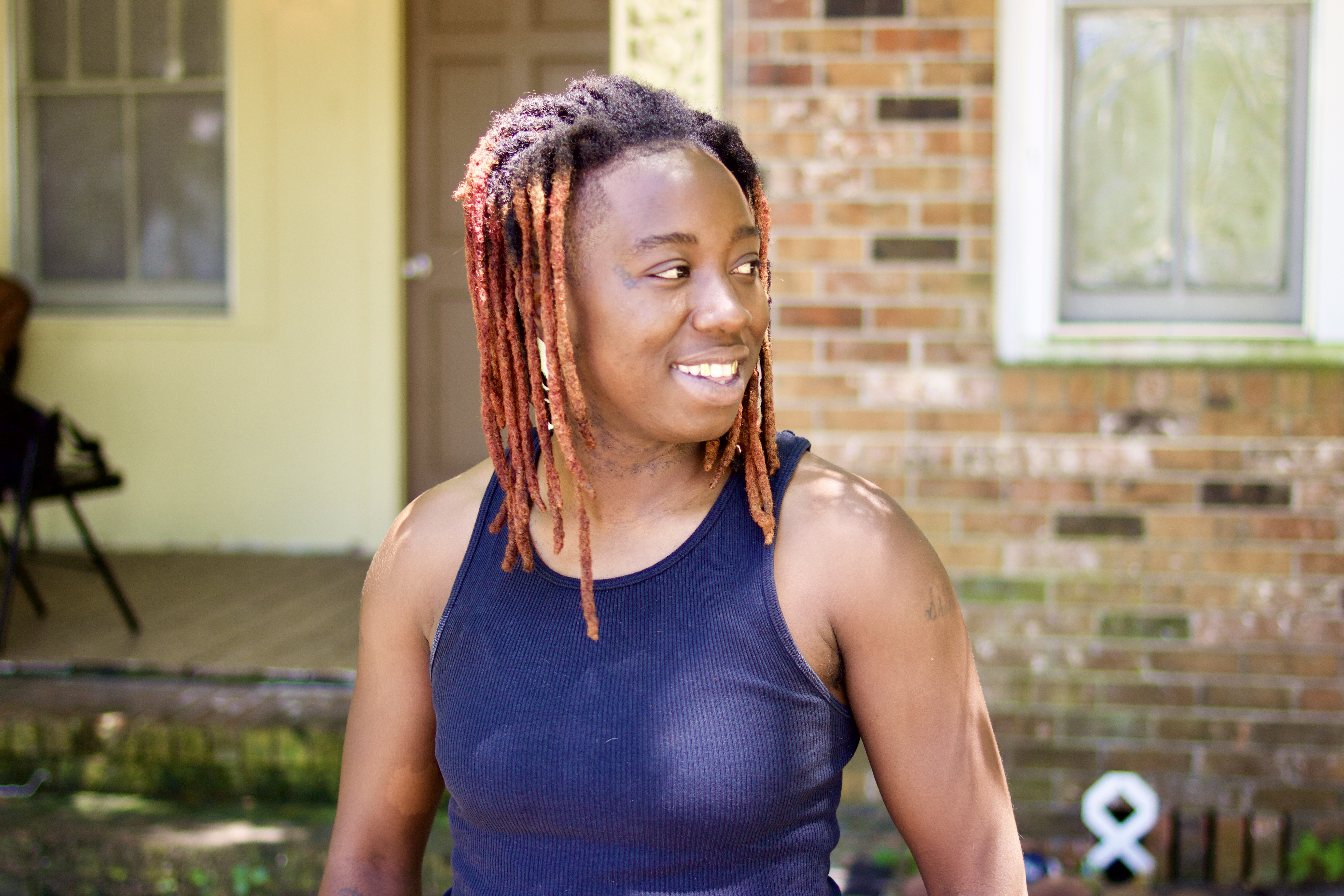 Shakira Williams standing in front of a brick building wearing a blue tank top. She is looking to the right of the frame and slightly smiling.