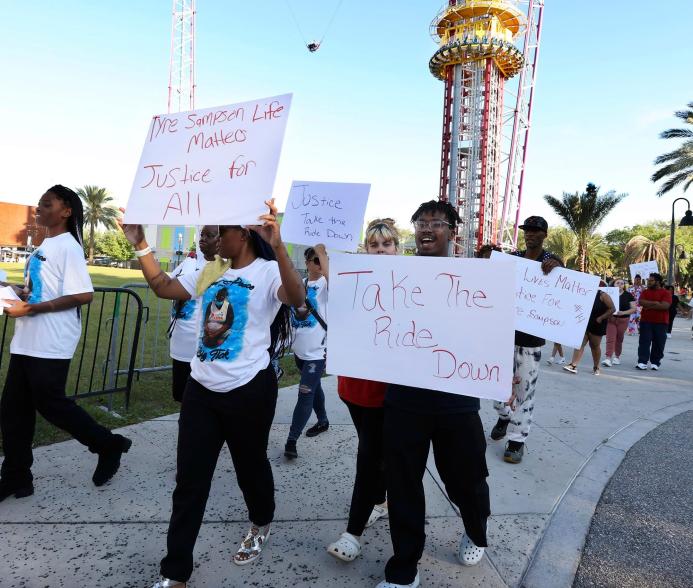 Family and supporters of Tyre Sampson march and hold signs outside the Orlando Free Fall drop tower ride at ICON Park in Orlando on Tuesday, March 29, 2022.