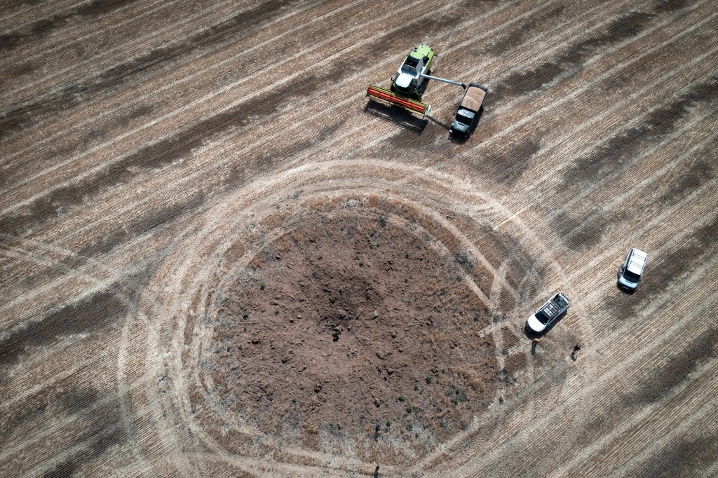 A farmer harvests grain in July near a crater caused by a Russian rocket in Ukraine. 