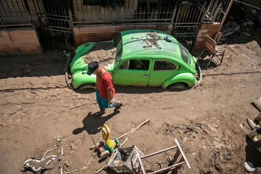 A person walks by a damaged car after a rain-fueled landslide