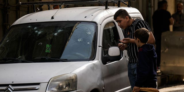 Palestinian kids look at a damaged car following an Israeli raid in the occupied West Bank city of Nablus, Tuesday, Oct. 25, 2022. The military says Israeli forces have raided a stronghold of an armed group in the West Bank, blowing up an explosives lab and engaging in a firefight. Palestinian health officials say five Palestinians were killed and 20 were wounded. The target of the raid was a group calling itself the Lions' Den, accused by Israel of having killed a soldier and attempting several attacks. 