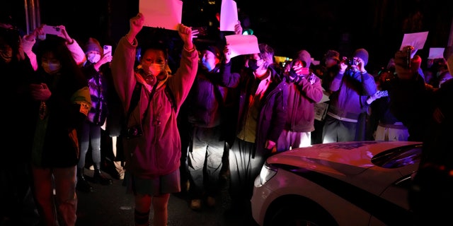 Protesters hold up blank pieces of paper and chant slogans as they march in protest in Beijing, Sunday, Nov. 27, 2022.