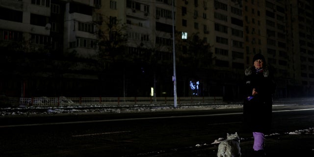 A woman with a dog waits for a bus in a street without electricity after critical civil infrastructure was hit by Russian missiles, in Kyiv, Ukraine Nov. 23, 2022.