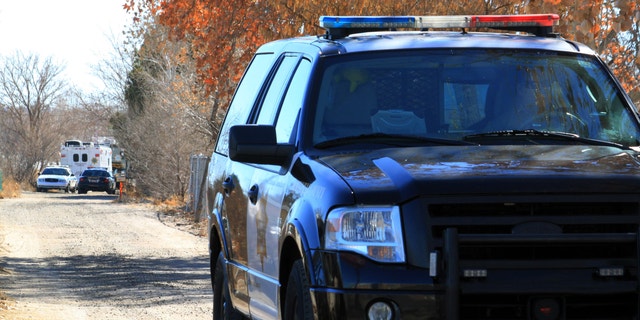 A Bernalillo County sheriff's deputy blocks the dirt road that leads to a home where detectives on Sunday, Jan. 20, 2013, were investigating the deaths of five people who were shot to death south of Albuquerque, N.M.