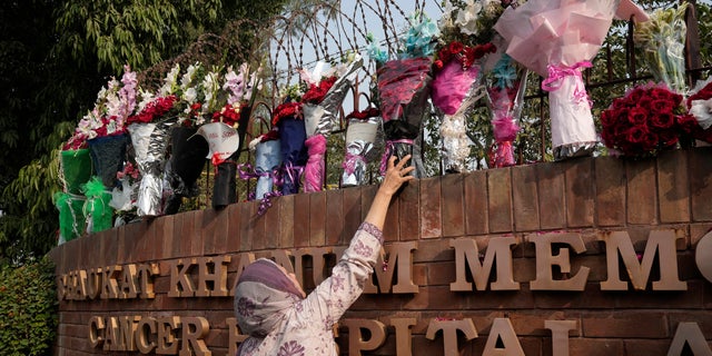 A woman places bouquet over the wall of a hospital where former Pakistani Prime Minister Imran Khan is being treated for a gunshot wound in Lahore, Pakistan, Friday, Nov. 4, 2022.