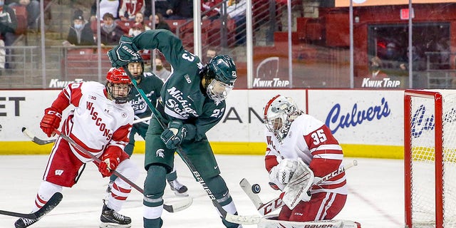 Wisconsin goalie Jared Moe, #35, makes a save while Michigan State forward Jagger Joshua, #23, looks for a rebound during a college hockey match between the University of Wisconsin Badgers and the Michigan State University Spartans on Jan. 14, 2022 at the Kohl Center in Madison, Wisconsin.