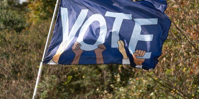 A flag reading VOTE waves as Sen. Raphael Warnock, D-Ga., meets with community members to encourage them to come out and vote on the first day of early voting on Oct. 17, 2022, in Duluth, Georgia. 