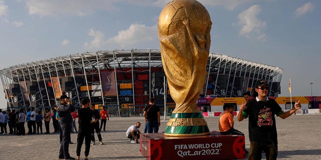 People pose for photos next to a giant replica on the World Cup trophy in front of Stadium 974 on November 18, 2022 in Doha, Qatar, ahead of the Qatar 2022 World Cup football tournament. 