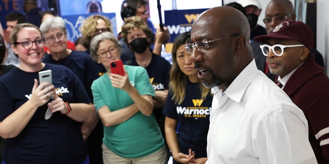 Sen. Raphael Warnock speaks to supporters as film director Spike Lee (R) listens during a canvass launch on Nov. 6, 2022, in Savannah, Georgia.