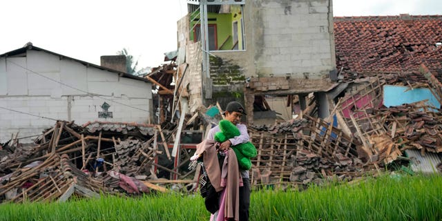 A man carries belongings salvaged from the ruins of his earthquake-damaged house in Cianjur, West Java, Indonesia Tuesday, Nov. 22, 2022. 