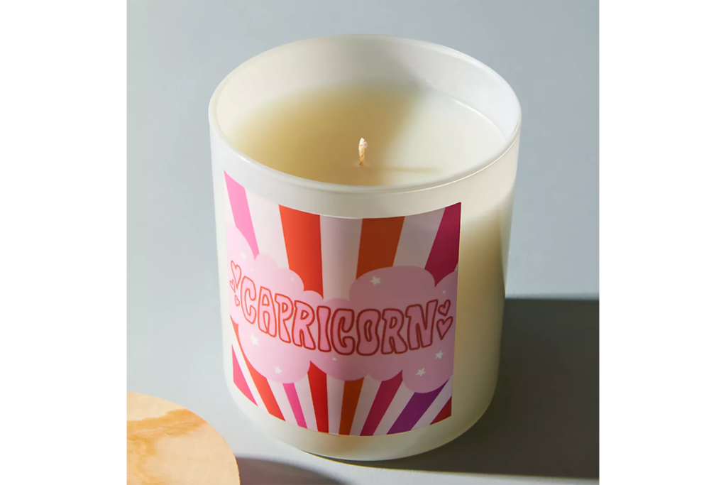 A white candle with pink label that reads Capricorn 