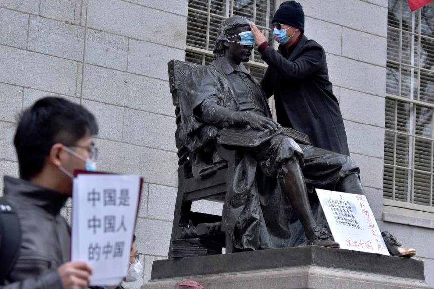 A man places a mask over the eyes of the John Harvard Statue in Harvard Yard as close to 100 students and faculty demonstrated against China's strict anti-virus measures on Nov. 29, 2022, at Harvard University.