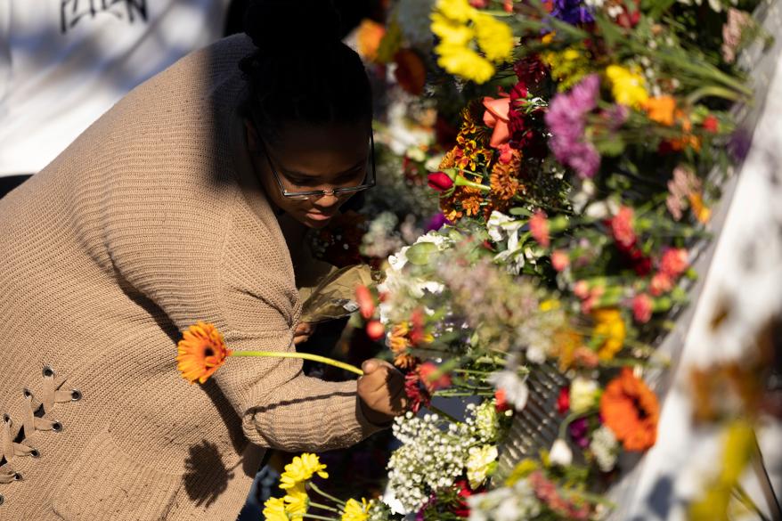A person places a flower on a memorial before a memorial service in Charlottesville, Va., Saturday, Nov. 19, 2022.