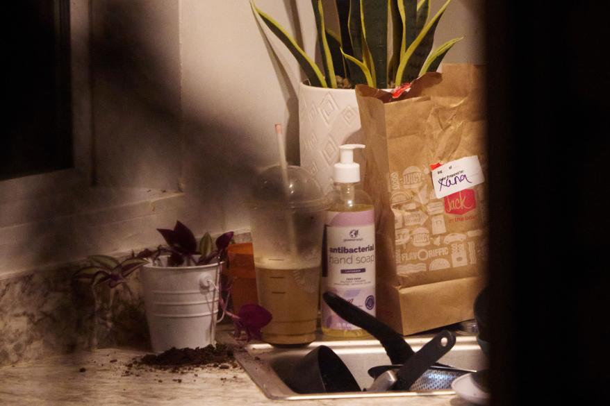 A paper bag containing a food order from Jack in the Box pis visible in a kitchen as investigators gather evidence at an off-campus home