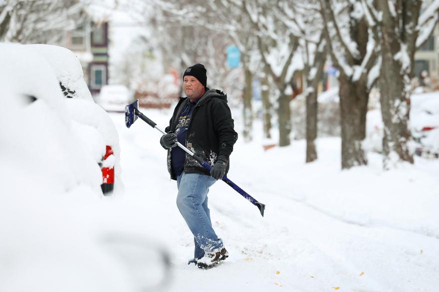 A picture of a man cleaning his vehicle during a snowstorm.