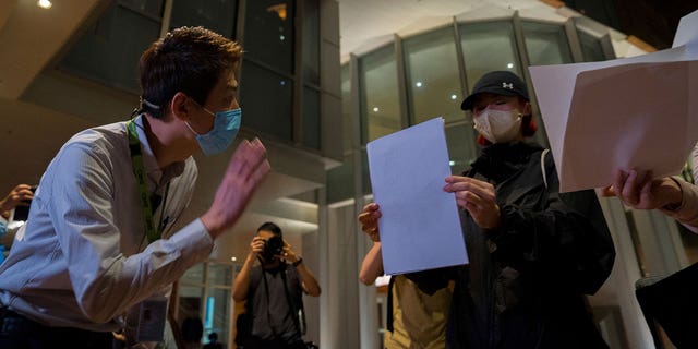 A University staffer checks the identity of protesters during a protest gathering at the University of Hong Kong in Hong Kong, Tuesday, Nov. 29, 2022. On Tuesday, about a dozen people gathered at the University of Hong Kong, chanting against virus restrictions and holding up sheets of paper with critical slogans. Most were from the mainland, which has a separate legal system from the Chinese territory of Hong Kong, and some spectators joined in their chants. 