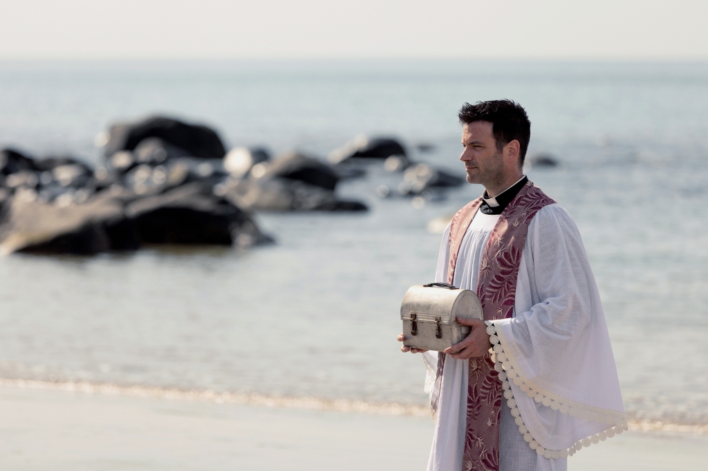 Colin Donnell holding a box on a beach. 