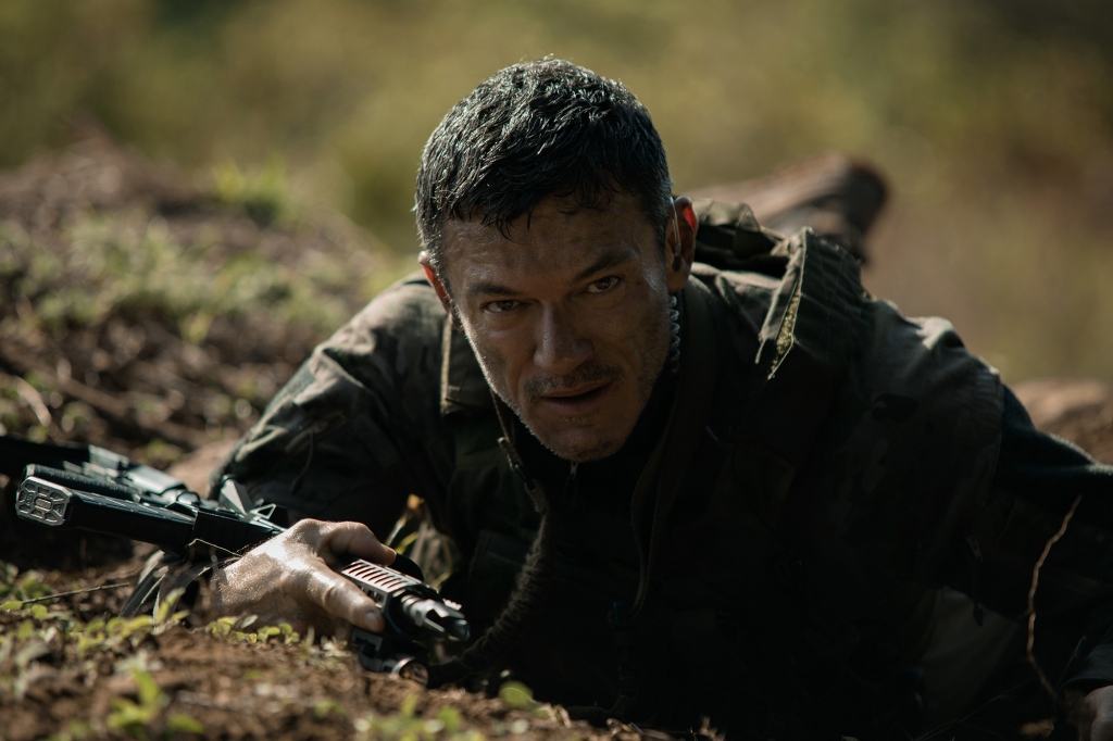 Bambi (Luke Evans) in "Echo 3" crouched on the ground with a gun. 