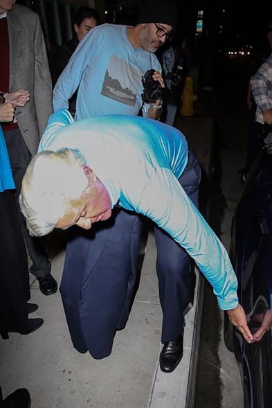 A picture of Jay Leno looking at his car after colliding with a police car.