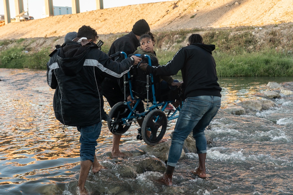 Asylum seekers cross the border into El Paso, helping a wheelchair bound child over the Rio Grande.