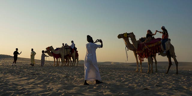 A tour guide takes a photo of a couple atop camels in Mesaieed, Qatar, Nov. 26, 2022. Throngs of World Cup fans in Qatar looking for something to do between games are leaving Doha for a classic Gulf tourist experience: riding a camel in the desert. But the sudden rise in tourists is putting pressure on the animals, who have almost no time to rest between each ride. 