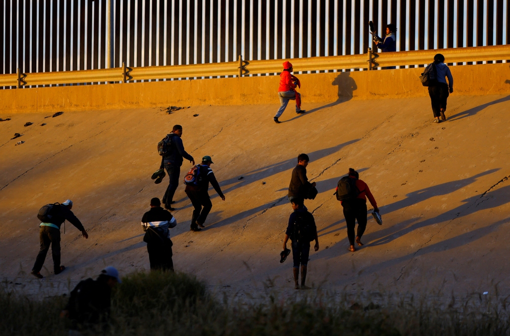 Migrants attempt to cross a barrier at the US-Mexico border