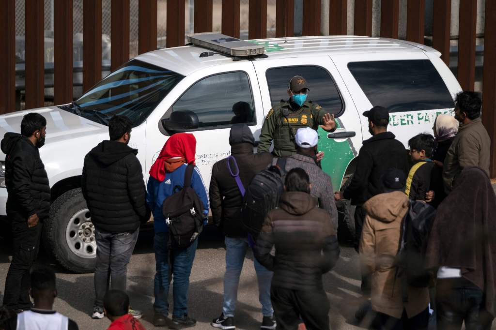 A border patrol agent talks to a group of migrants, mostly from African countries, before processing them after they crossed the US-Mexico border, taken from Tijuana, Baja California state, Mexico, on November 11, 2022. (Photo by Guillermo Arias / AFP) (Photo by GUILLERMO ARIAS/AFP via Getty Images)
